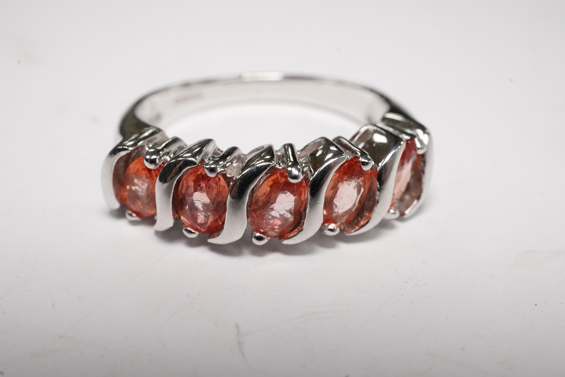 A modern 18ct white gold and five stone orange/pink stone set half hoop ring, size M/N, gross weight 5.6 grams. Condition - fair to good